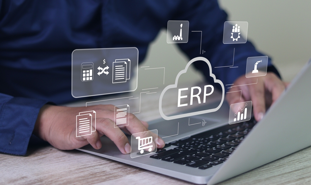 Hands typing on a laptop with ERP cloud icons representing business functions like finance, inventory, sales, and manufacturing.
